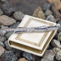 This pretty circa 1920s platinum brooch features a pierced design with engraved details and bordered with milgrain edging. The brooch is accented with seventeen (17), bead set, old European cut diamonds and eighteen (18), channel set, rectangular French cut synthetic blue sapphires. The brooch measures 65.7mm in length and 7.0mm in width. The brooch is finished with a 14K white gold pin stem and catch. Platinum Brooch Jewelry For Anniversary, Art Deco Platinum Brooches In White Gold, Vintage Platinum Brooches For Anniversary, Art Deco White Gold Brooch In Platinum, Art Deco Platinum Brooch For Formal Occasions, Art Deco White Gold Platinum Brooches, Platinum Art Deco Brooch For Formal Occasions, Formal Art Deco Platinum Brooches, Vintage Platinum Brooches With Diamond Accents