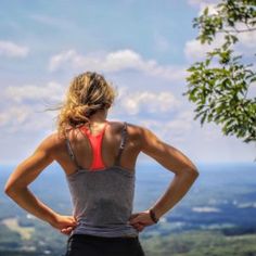 a woman standing with her back to the camera looking out over a valley and mountains