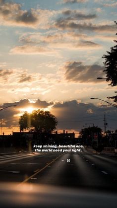 the sun is setting over an empty street with clouds in the sky and trees on either side