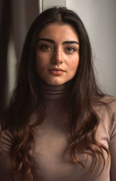 a woman with long brown hair wearing a turtle neck shirt and standing in front of a window