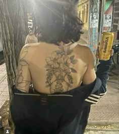 a woman with tattoos on her back holding a beer