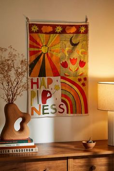 a wooden table topped with books and a vase filled with flowers next to a wall hanging