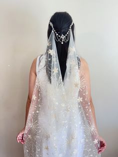 a woman wearing a veil with flowers and chains on it's head is standing in front of a white wall