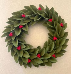 a green wreath with red berries hanging on the front and side of it, sitting on a white surface