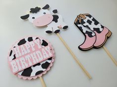 a cow cake topper sitting on top of a table next to two cupcakes