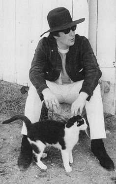 black and white photograph of a man sitting on a bench with a cat in front of him