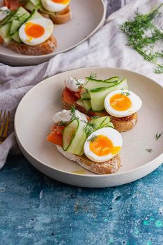 two plates filled with sandwiches topped with eggs and cucumber on top of bread