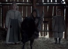 two children standing next to a goat in a barn