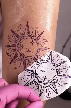 a person holding up a piece of paper with a sun and moon tattoo on it