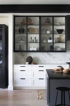 a black and white kitchen with marble counter tops, open cabinet doors, and stools