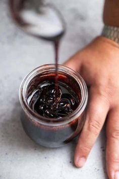 a person holding a jar filled with liquid on top of a white table next to a spoon