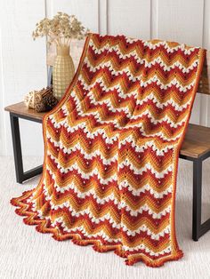 an orange and white crocheted blanket sitting on top of a bench next to a vase