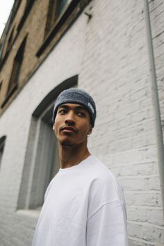 a young man standing in front of a white brick building wearing a beanie hat