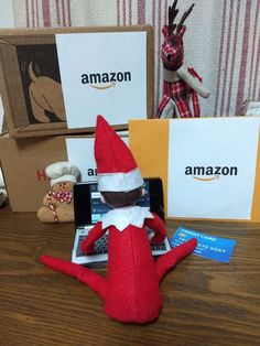 an elf sitting on top of a laptop computer next to two boxes with amazon's logo