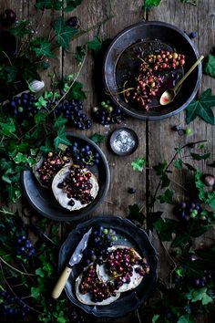 two bowls filled with food on top of a wooden table next to grapes and leaves