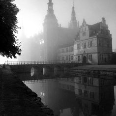 an old castle with water and bridge in the foreground on a foggy day