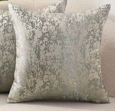 two silver sequin pillows sitting on top of a white couch next to a potted plant