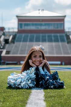 a cheerleader laying on the ground in front of a football field with her pom poms