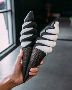 a hand holding two ice cream cones in front of a window with black and white stripes