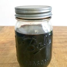 a mason jar filled with black liquid sitting on top of a wooden table next to a white wall