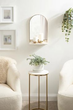 two white chairs and a table in a room with pictures on the wall behind them