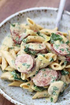 pasta with sausage and spinach in a white bowl on top of a wooden table