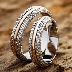 two tone gold and silver wedding rings on top of a piece of wood with one ring in the middle