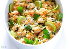 a white bowl filled with shrimp and rice topped with cilantro, limes and parsley