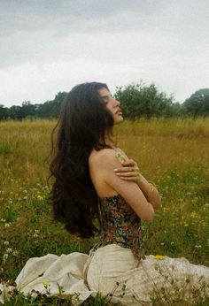 a woman with long hair sitting in the grass