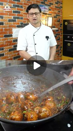 a man cooking food in a pan on top of a stove next to a brick wall