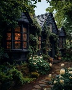 a house that is surrounded by greenery and flowers in front of the windows, along with stone walkway leading up to it