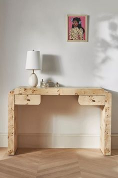 a wooden table with a lamp on top of it in front of a white wall