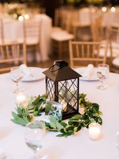 a lantern on top of a table surrounded by greenery and lit candles at a wedding reception