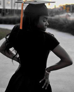 a young woman wearing a graduation cap and gown, standing on the sidewalk with her hands behind her back