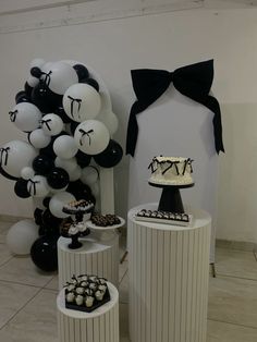 black and white desserts are displayed on pedestals in front of the wall with balloons