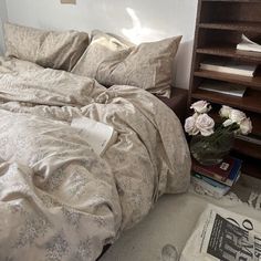 an unmade bed in a small room with bookshelves and flowers on the floor