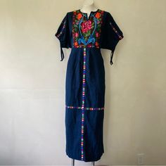 Great Pre-Owned Condition, No Defects Other Than Some Minor Signs Of Use. Beautiful Vintage Circa 1970s Guatemalan Huipil-Style Maxi Folk Dress, In A Dark Indigo Blue With Colorful Woven Designs. It Has A Pull-On Fit With No Closures, And A Low Waist With An Attached Tie - When You Tie It At The Back Of Your Natural Waist, It Cinches Up The Bodice For A Blouson Effect. It Has Half-Length Dolman Sleeves That Cinch, A Notched Neckline That Lies Open, And Pleating On The Front Of The Skirt. Mannequ Blue Embroidered Maxi Dress With Intricate Details, Blue Maxi Embroidered Dress With Intricate Embroidery, Blue Maxi Embroidered Dress With Intricate Details, Blue Folk Dress For Spring, Folk Style Embroidered Fitted Maxi Dress, Traditional Blue Maxi Dress With Floral Embroidery, Blue Fitted Folk Dress, Traditional Blue Dress With Geometric Embroidery, Blue Cotton Embroidered Maxi Dress