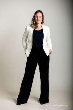 a woman in black pants and a white blazer posing for the camera with her hands on her hips