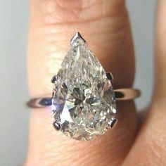 a close up of a person's hand holding a ring with a pear shaped diamond