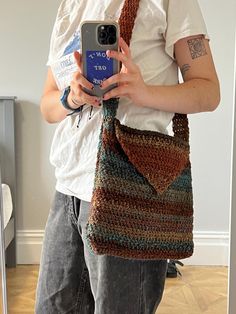 a man holding a cell phone and crocheted bag in front of his face