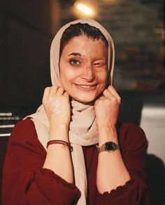 a woman wearing a headscarf smiles at the camera while holding her hands to her face