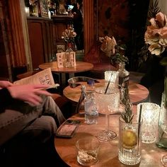 two people sitting at a table with glasses and bottles on it, one person is reading the paper