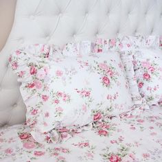 a white bed topped with lots of pillows and pink flowers on it's headboard