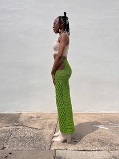 a woman standing in front of a white wall wearing a green crochet skirt