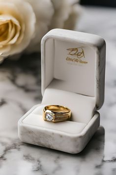 an engagement ring sits in a box on a marble table next to a rose flower