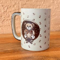 a white coffee mug with a brown bear on it's side sitting on a wooden table