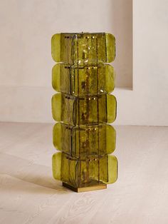 a tall green vase sitting on top of a wooden table next to a white wall