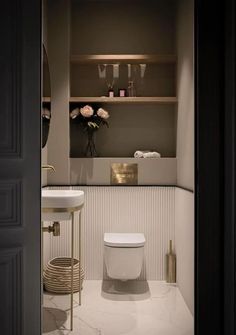 a white toilet sitting in a bathroom next to a sink and wooden shelves with vases