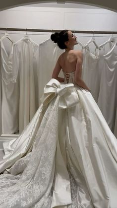 a woman in a wedding dress looking at the back of her gown, which is hanging on a rack