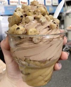 a person holding up a cup filled with ice cream and chocolate chip cookie doughnuts